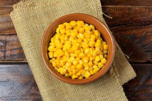 Raw corn kernels inside ceramic bowl on rustic wooden table. space for text photo