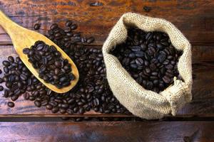 roasted and fresh coffee beans inside rustic fabric bag and poured over rustic wooden table photo