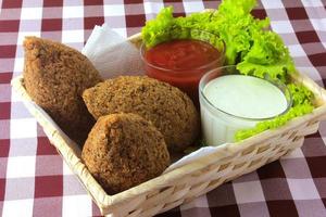 Kibbeh frito con salsa de tomate en una canasta, sobre una mesa de madera rústica foto