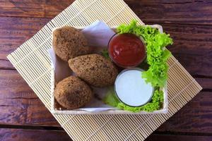 Kibbeh frito con salsa de tomate en una canasta, sobre una mesa de madera rústica foto