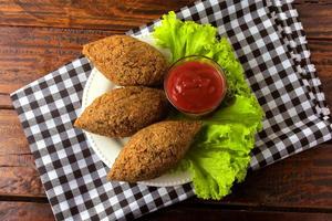 Fried kibbeh with tomato sauce on a plate, over rustic wooden table photo