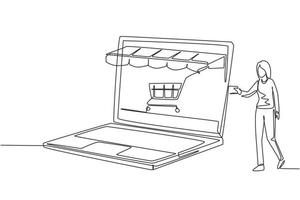 Continuous one line drawing young woman inserting credit card into large canopy laptop screen with shopping cart. E-shop, digital payment concept. Single line draw design vector graphic illustration