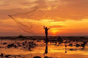 red de pesca de silueta este es un pescador de pie en un barco durante el amanecer en el lago udon thani, tailandia. foto