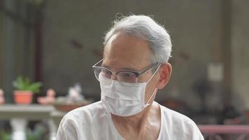 Elderly grandfather in eyeglasses wearing face mask looking around his house.