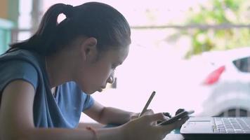 niña de la escuela mediante teléfono móvil durante la realización de la tarea. video