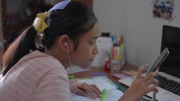 High school girl wears earphones watching lesson online on smartphone at home. video