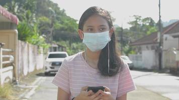 retrato chica usa máscara protectora escuchando y viendo las redes sociales en línea desde el teléfono inteligente. video