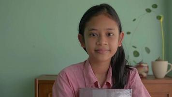 Portrait female teenager student holding a textbook while standing at home. video