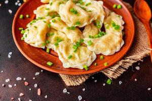 The boiled made dumplings with a stuffing with oil and green onions on a dark table photo