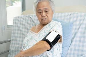 Asian senior old woman using wireless digital home measure blood pressure machine medical device to monitor heart health algorithm. photo