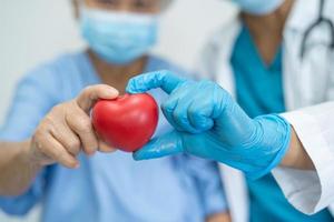 Doctor wearing ppe with mask give red heart for protect coronavirus to Asian senior or elderly old woman patient photo