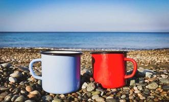 close up of sky blue and red cups on the rocks in the beach with calm sea in the background. photo