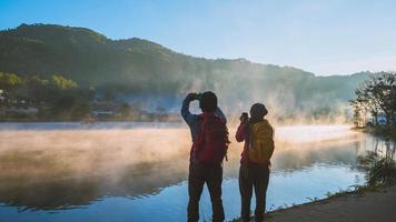 mujer asiática y hombre asiático que mochilero de pie cerca del lago, ella estaba sonriendo, feliz y disfrutando de la belleza natural de la niebla. foto