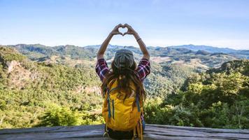 Joven turista con mochilas felices de viajar levantó la mano para hacer una forma de corazón y disfrutar del paisaje natural de la montaña. foto