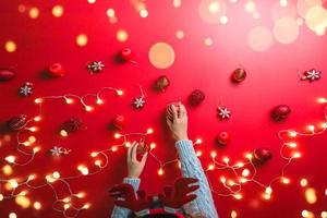 la niña está usando la mano para sostener la bola adornos rojos sobre un fondo rojo con adornos navideños con luz led. vista superior. tradiciones familiares navideñas. concepto de navidad. foto