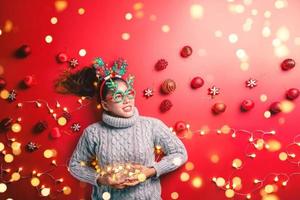 Christmas New Year. Young Woman dressed in warm sweater with  Props ball red with christmas ornaments in Holiday on shine red background. Concept merry christmas. photo