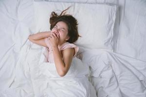 Young woman sleeping well in bed hugging soft white pillow. Teenage girl resting. good night sleep concept. Girl wearing a pajama sleep on a bed in a white room in the morning. warm tone. photo