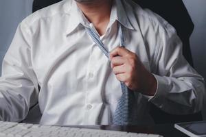 Close up portrait of exhausted frustrated stressed handsome sad unhappy upset entrepreneur trying to take off uncomfortable tie formal wear isolated at office., tired businessman taking off necktie. photo