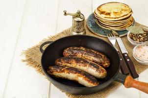 Grilled sausages, pancakes on white wooden table. photo