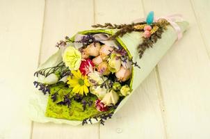 Bouquet of flowers wrapped in paper on white wooden table photo