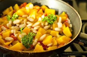 Guiso de verduras con calabaza y frijoles blancos en sartén foto