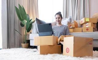Online Marketing, Young start up small business owner writing address on cardboard box from list order. small business entrepreneur SME or freelance asian woman working with box at home photo