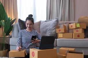 marketing en línea, joven emprendedor propietario de una pequeña empresa escribiendo la dirección en una caja de cartón del orden de la lista. Pyme empresario de pequeñas empresas o mujer asiática independiente que trabaja con caja en casa foto