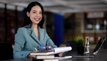joven mujer de negocios asiática hermosa encantadora sentada sonriente trabajando en la oficina. mirando a la cámara. foto
