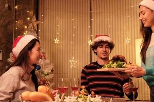 una comida especial para la familia, la joven sirve pavo asado a los amigos y alegre con bebidas durante una cena en el comedor de la casa decorado para el festival de Navidad y la fiesta de celebración de año nuevo. foto