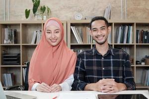 Portrait of entrepreneur of business startup, young male and beautiful female owner, two partners Islamic people, looking at camera, smiles happily in small e-commerce workplace office. photo