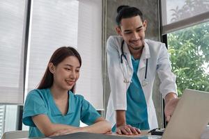 Healthcare team partners. Two uniformed young Asian ethnicity doctors are co-workers discussing medication in hospital's clinic office. Specialist persons are experts and professionals. photo