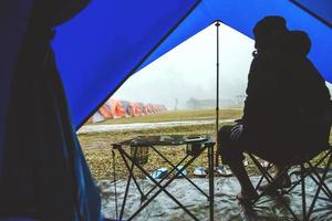 viaje de hombre asiático relajarse en las vacaciones. acampar en la montaña. siéntate, relájate en la silla. en la atmósfera, la lluvia cae tiene niebla. tailandia foto