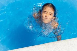 linda niña de ocho años jugando en una piscina. foto