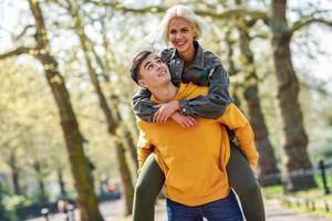 Funny couple in a urban park. Boyfriend carrying his girlfriend on piggyback.