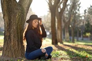 Thoughtful woman sitting alone outdoors wearing hat photo