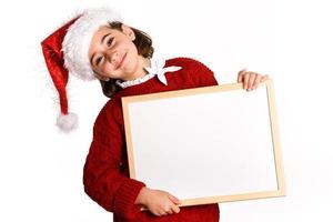 Little girl wearing santa hat holding blank board photo