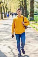 Young urban man using smartphone walking in street in an urban park in London.