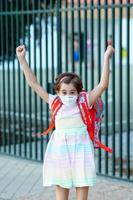 Girl wearing a mask takes a jump for joy at going back to school. photo