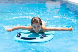 Cute girl playing with a bodyboard in a swimming pool. photo