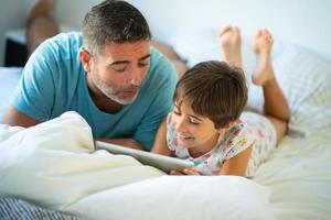Middle-age father with her eight years daughter using digital tablet in bedroom. photo