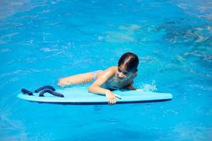Cute girl playing with a bodyboard in a swimming pool. photo