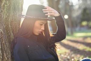 Thoughtful woman sitting alone outdoors wearing hat photo