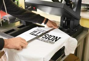 Young man printing on t-shirt at workshop photo