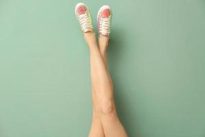 Legs of young woman in stylish casual shoes on color background photo