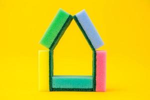 Esponjas multicolores para limpieza dobladas en forma de casa sobre un fondo amarillo