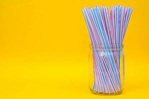 Plastic straws in a glass jar with yellow background photo