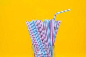 Plastic straws in a glass jar with yellow background photo
