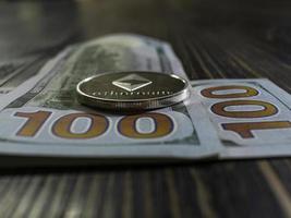 Silver Ethereum on US dollars. Digital currency close-up on a wooden background.Real coins of bitcoin on banknotes of one hundred dollars photo