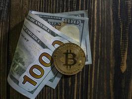 Golden Bitcoin on US dollars. Digital currency close-up on a wooden background.Real coins of bitcoin on banknotes of one hundred dollars photo