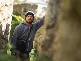 bearded man in knitted hat and jacket with hood posing in a ravine of a fortress